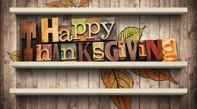 Happy Thanksgiving spelled out in colorful, wooden block letters on a shelf, with autumn leaves behind, against a rustic wooden background.