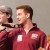 A young man in a maroon jacket holding a microphone speaks on stage. Another person wearing a cap stands beside him. The man’s jacket reads “SCC Members” and “Homecoming Committee,” identifying him as David LaVanne.