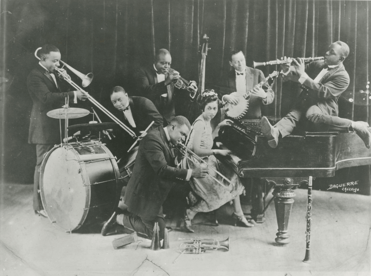 King Oliver's Creole Jazz Band, left to right: Honoré Dutrey, trombone; Warren “Baby” Dodds, drums; “King” Joe Oliver, cornet; Louis Armstrong (kneeling in front), slide trumpet; Lil Hardin Armstrong, piano; Bill Johnson, banjo/bass; Johnny Dodds, clarinet. Photo: Hogan Jazz Archive Photography Collection, Tulane University Libraries