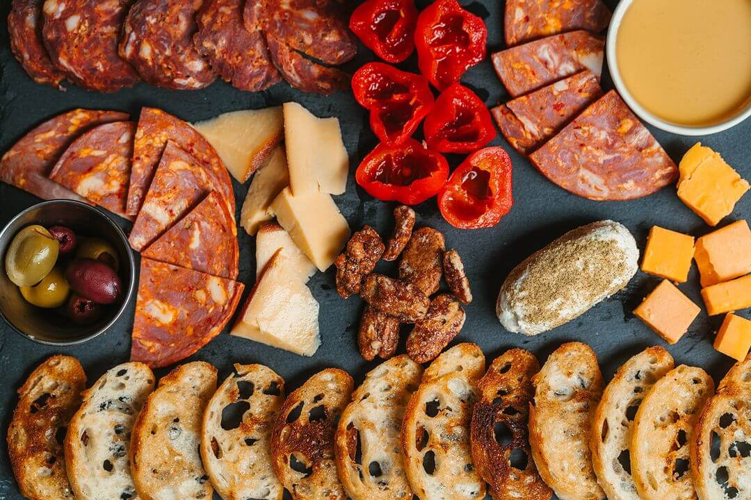 charcuterie board with meats, vegetables, bread, cheeses, and olives