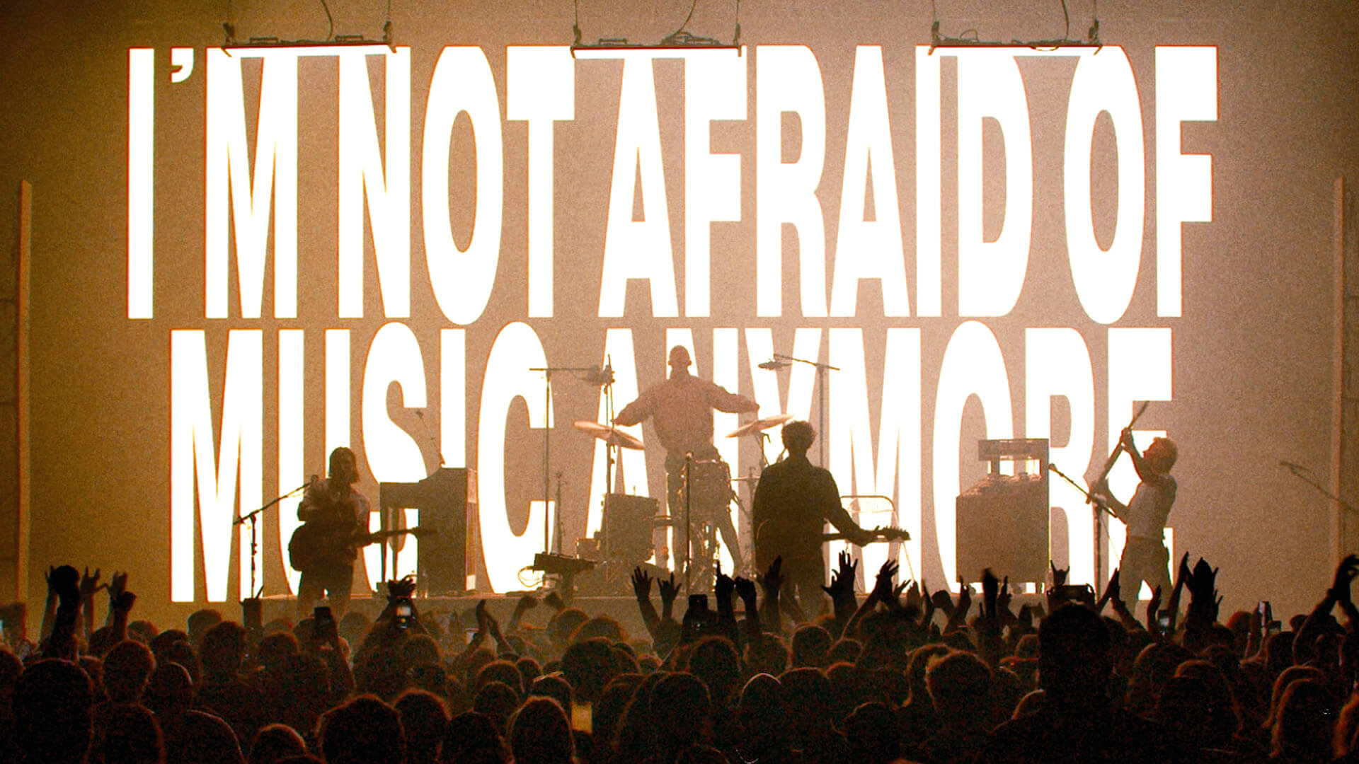 COIN the band on stage with the phrase "I'm not afraid of music anymore" projected on a screen