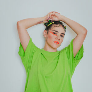 Pahua, a musician from Mexico, wearing a green shirt. Her face is adonred with colorful paint.