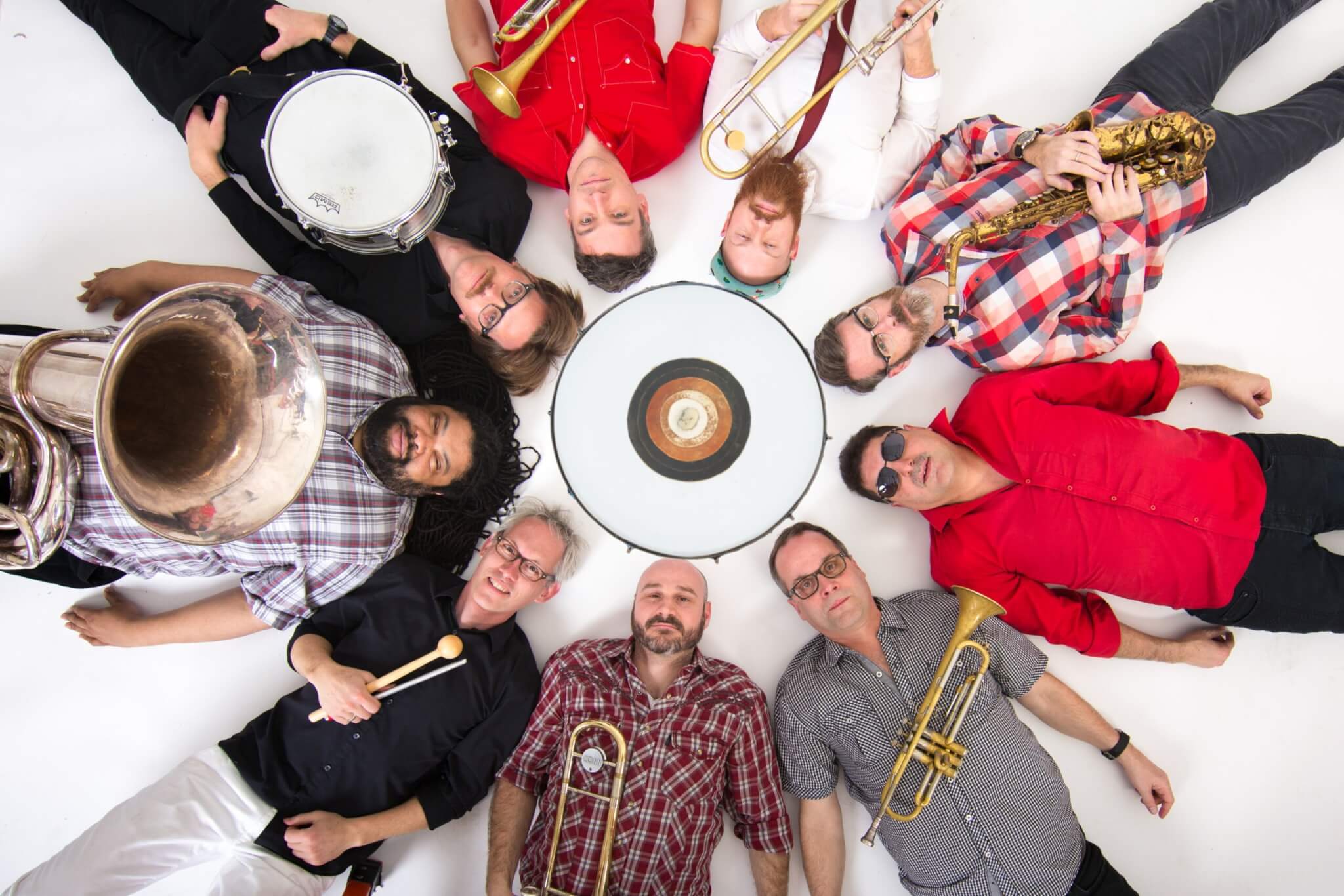 Members of Slavic Soul Party lying down in a circular formation holding instruments
