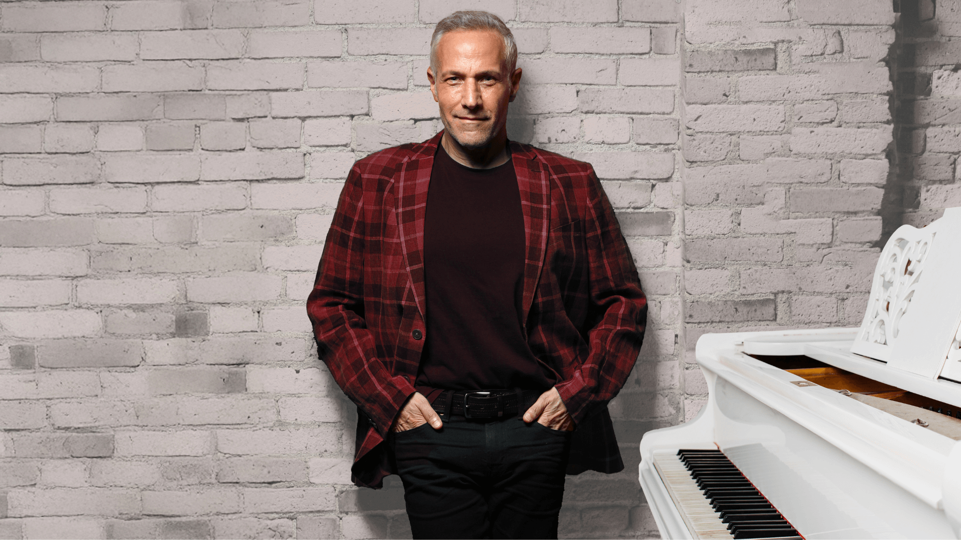 Jim Brickman against brick wall with white piano