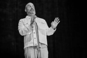 Tom Segura on stage, gesturing with a microphone
