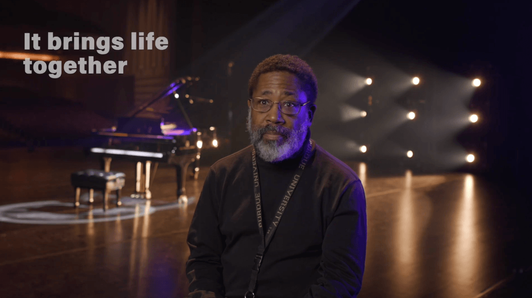Friends of Convos member Barrett Caldwell on stage in front of a piano speaking about the importance of Purdue Convocations to the community - "it brings life together."