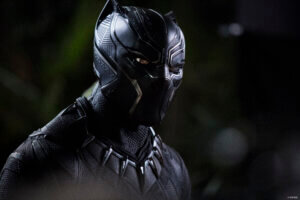 A person dressed in a Black Panther superhero suit with silver accents and a stylized mask stands against a dark, blurred background, channeling the power and presence of the hero as if ready for a Live In Concert appearance.