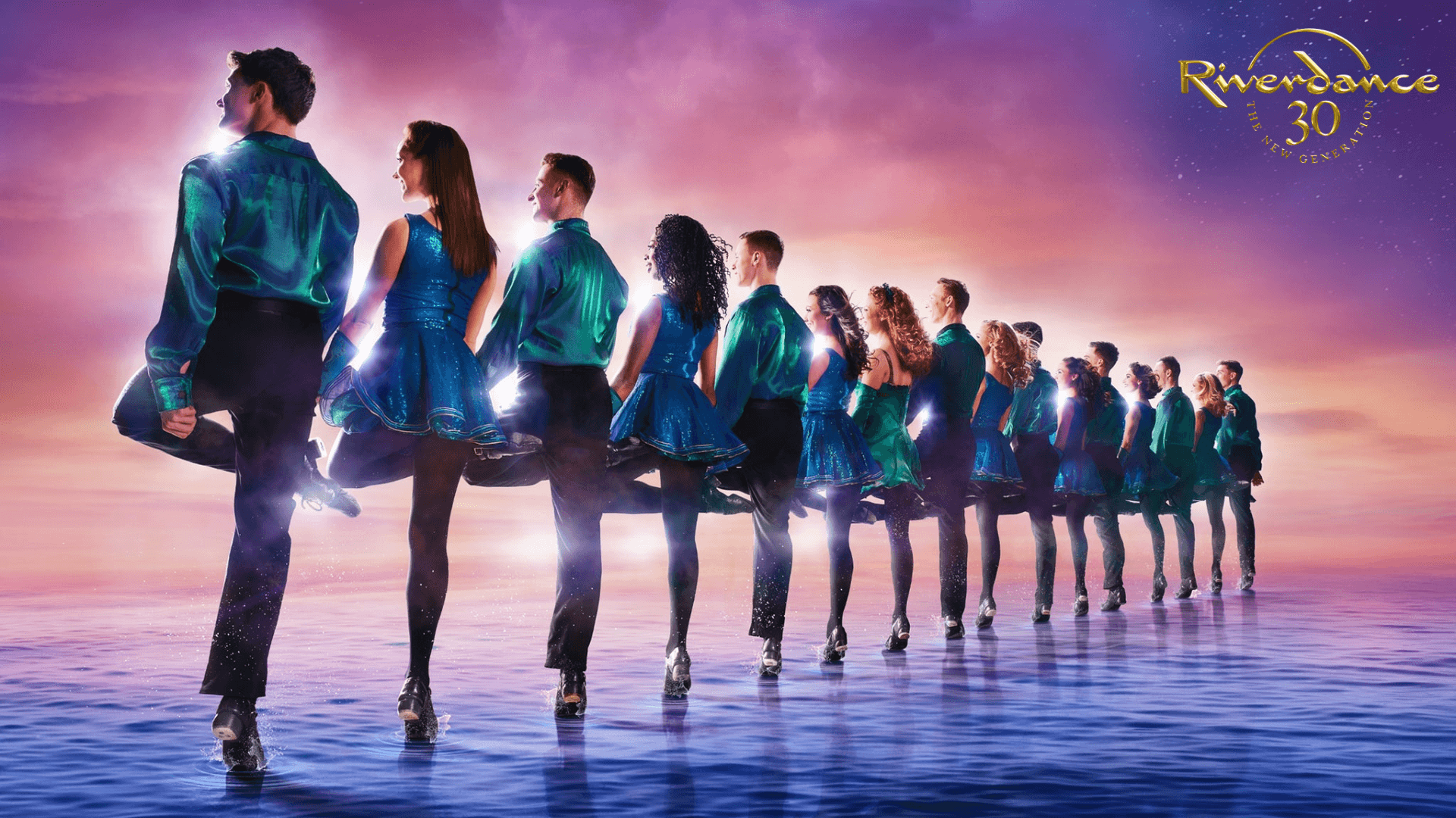 A row of dancers in sparkling blue and green costumes perform a high-kick routine on a reflective surface under a colorful sunset sky, with the Riverdance 30th Anniversary logo in the top right corner.