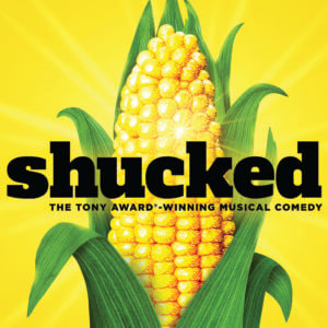 A bright yellow ear of corn with green husks is set against a yellow background. Bold black text reads shucked, and below in yellow text: The Tony Award-winning musical comedy.