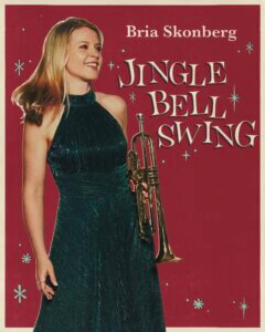 A woman in a dark green sleeveless dress holds a trumpet and smiles. The background is red with white star accents. Text reads: Bria Skonberg Jingle Bell Swing.