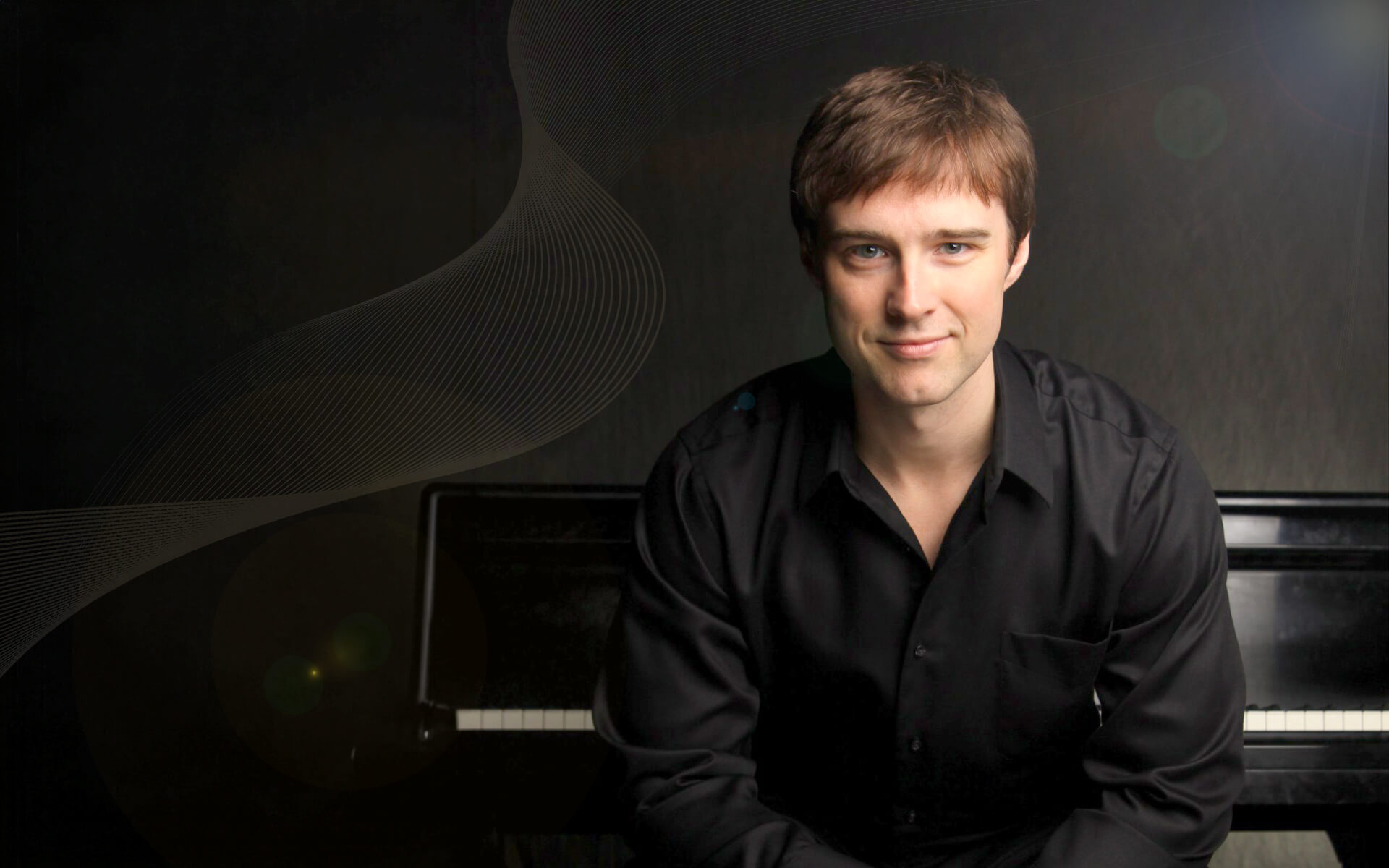 A young man in a black shirt sits in front of a piano, smiling softly. The background is dark with subtle abstract lines and light flares, creating a modern, artistic atmosphere.